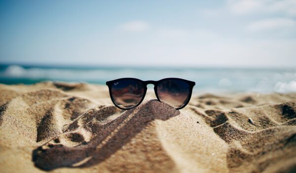 Un paio di occhiali da sole sopra una duna di sabbia con sullo sfondo il mare