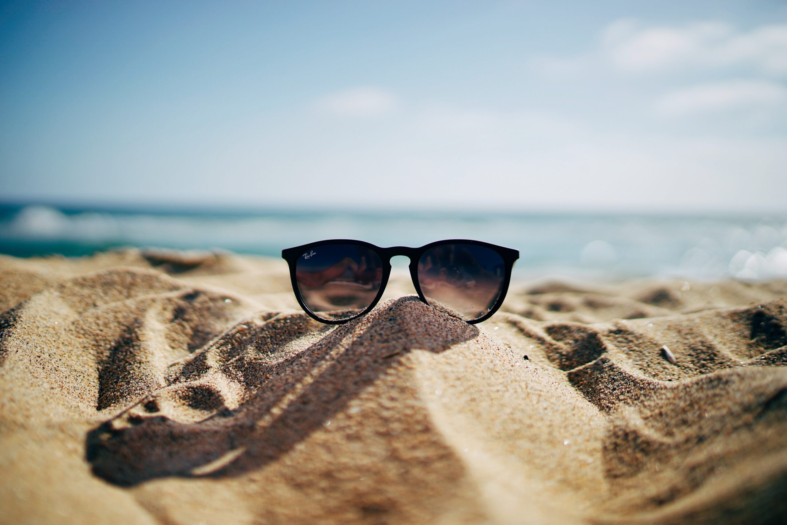 Un paio di occhiali da sole sopra una duna di sabbia con sullo sfondo il mare
